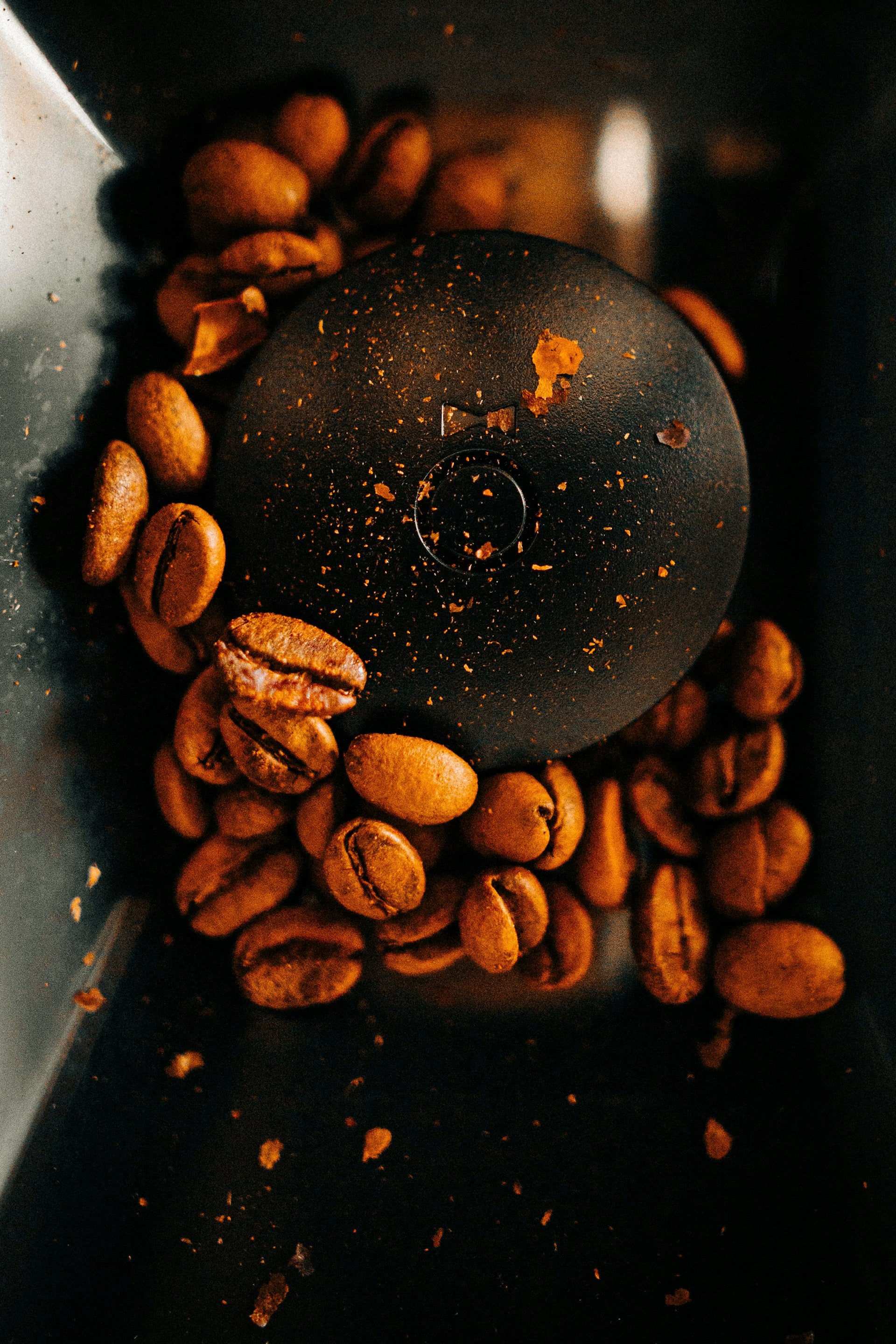Close-up view of coffee beans inside a grinder, with a visible circular grinding mechanism in the center. Coffee grounds and bean fragments are scattered around, showing the grinding process in action.