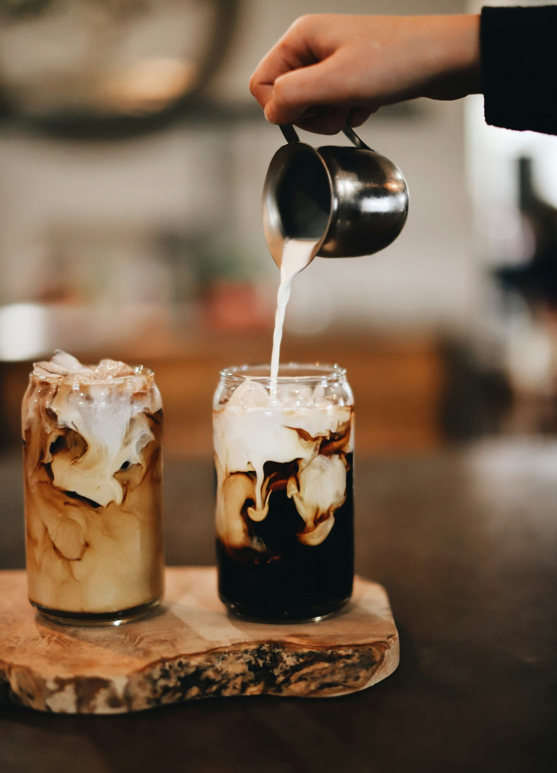 Iced coffee with milk being poured into glass on wooden board