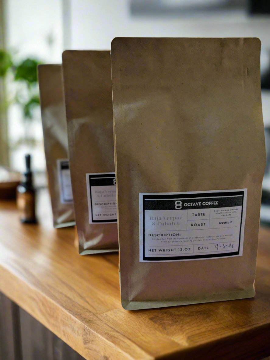 Three brown bags of Octave Coffee's Baja Verapaz & Cubulco medium roast coffee, neatly lined up on a wooden counter, showcasing their minimalist packaging with detailed labels.